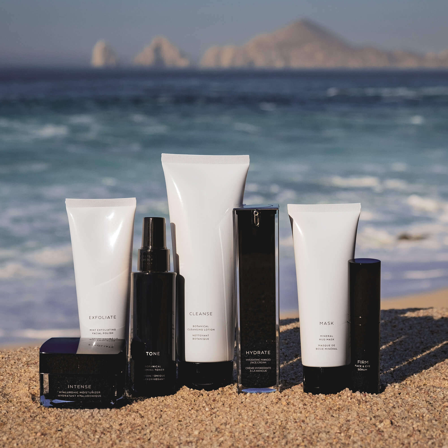 Assorted MIANIMED premium skincare products displayed on a beach with ocean and mountains in the background